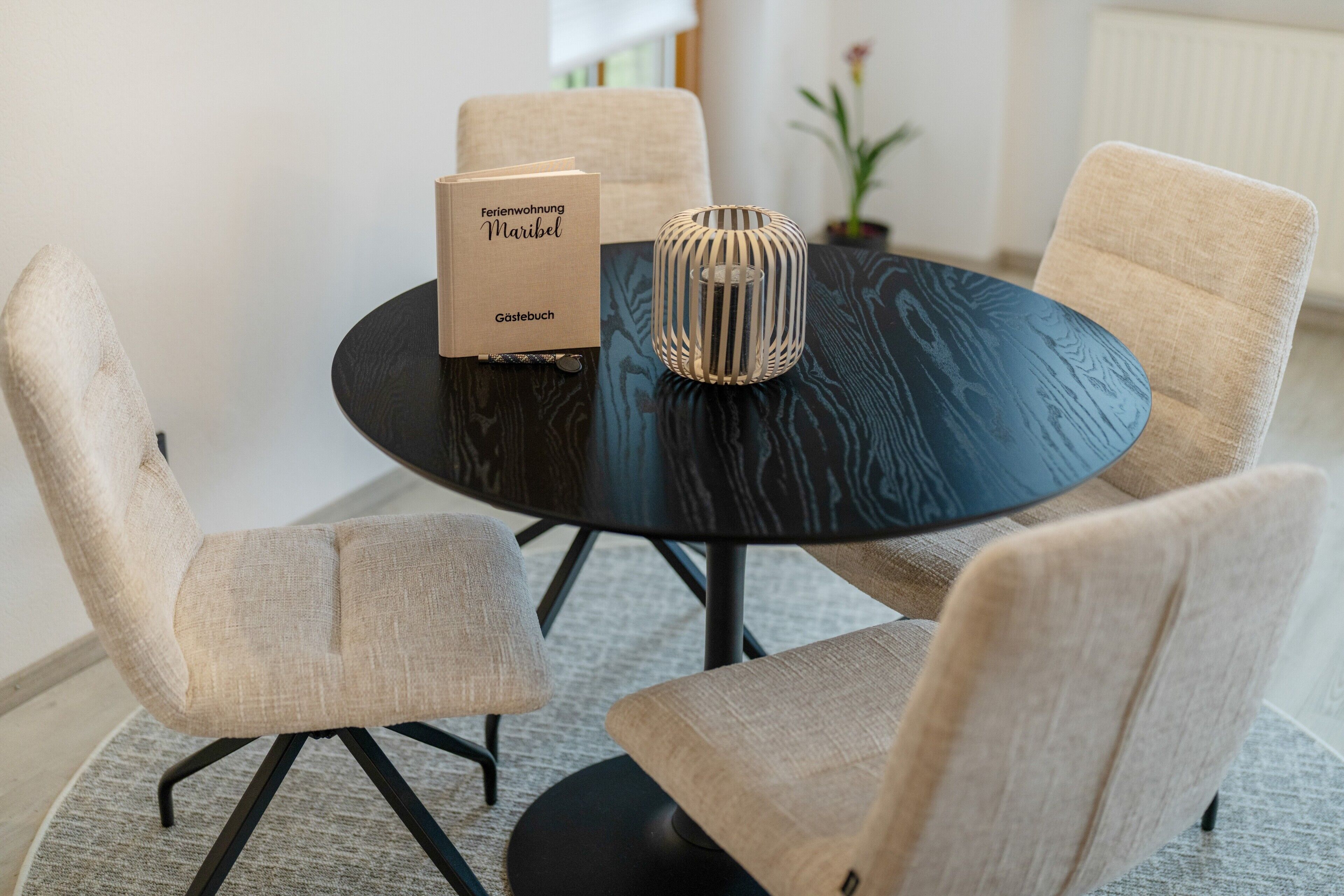 Ein runder Tisch mit zwei Stühlen, einer dekorativen Vase und zwei Büchern mit dem Titel 'Ferienwohnung Maribel' auf einer dunklen Tischdecke.