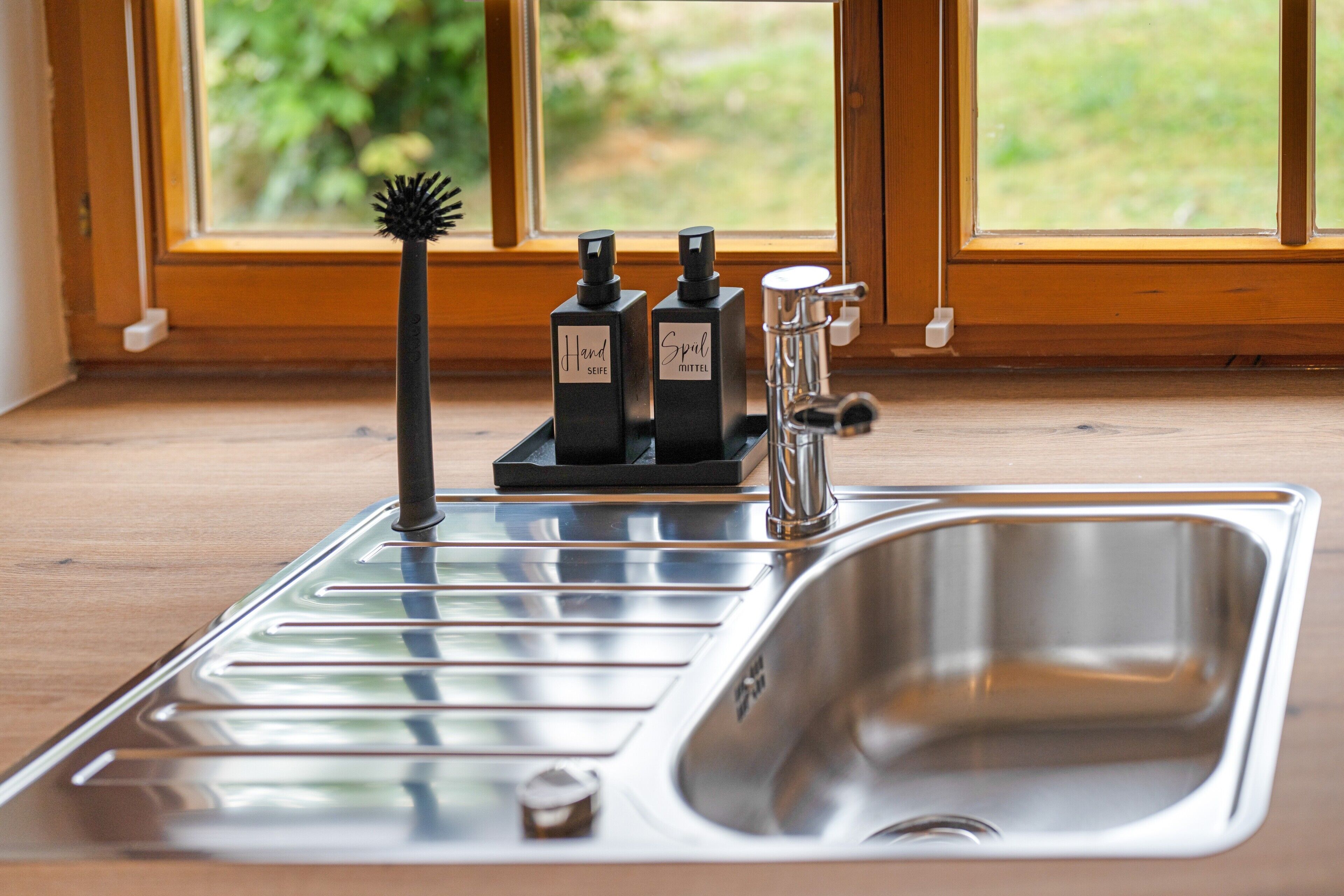 Ein Küchenspülbecken mit einem modernen Wasserhahn, eine Handseifenflasche und eine Desinfektionsmittel-Flasche.