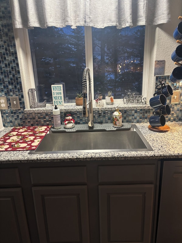 A kitchen with a stainless steel sink, a window with a view of trees, and holiday decorations. - Beautiful, cozy 3 bedroom, two bath, private home on acreage in the mountains (Lava Hot Springs)