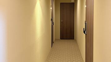 Un pasillo con piso alfombrado, puertas de madera y luminarias fijadas a la pared.