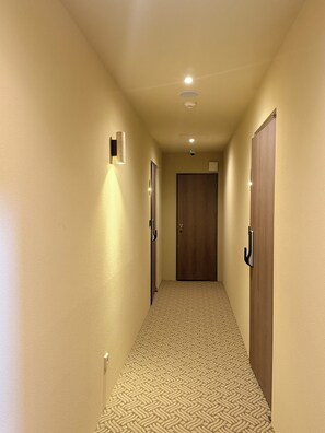 A hallway with carpeted flooring, wooden doors, and wall-mounted light fixtures.