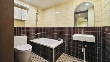 Baño con bañera, inodoro y lavamanos, que presenta un piso con diseño de cuadros y paredes con azulejos en tonos oscuros y claros.