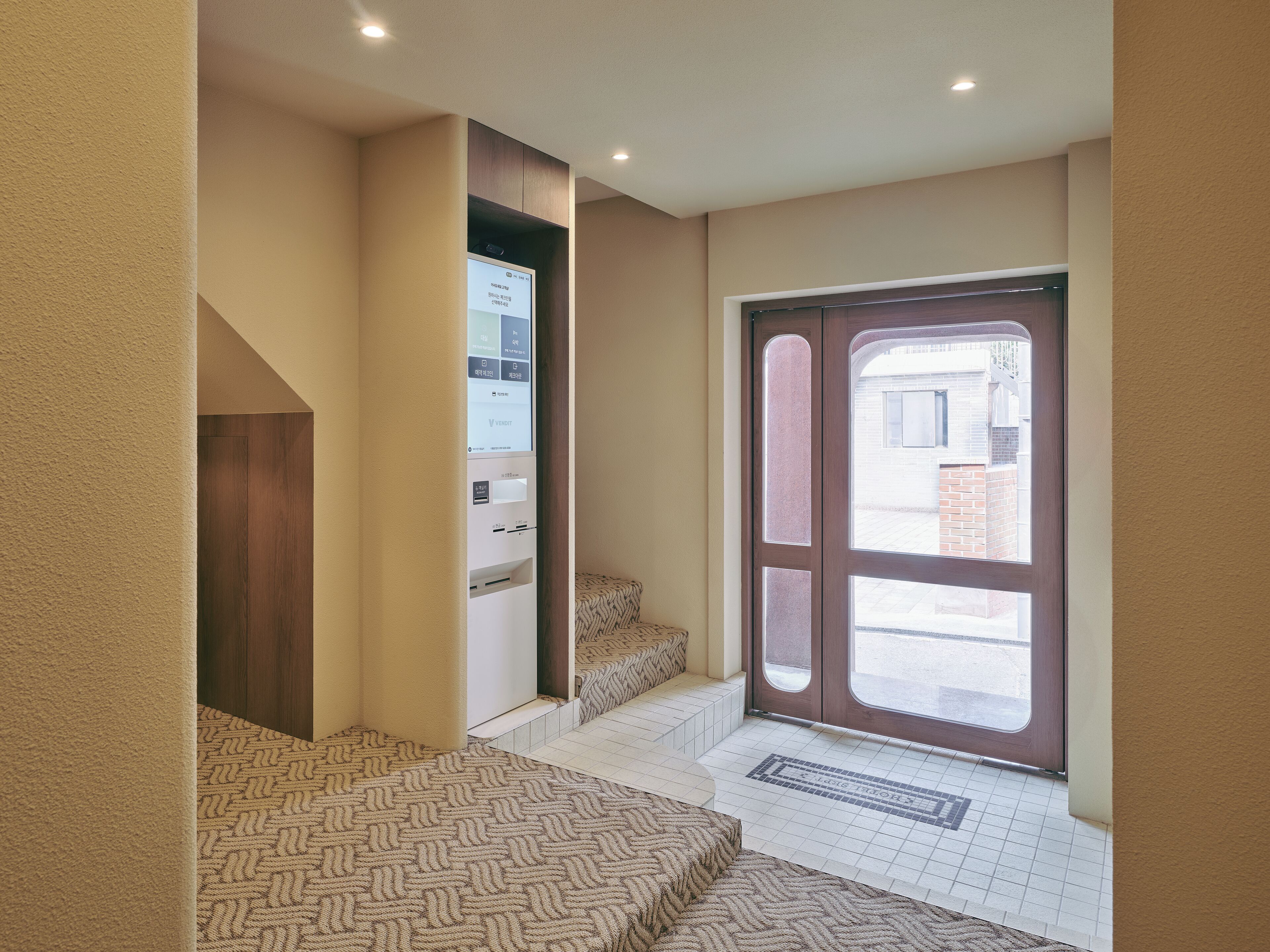 A hotel entrance with a digital display, a set of stairs, and a door leading outside.
