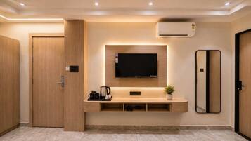 A modern hotel room with a flat-screen TV mounted on a wooden wall, a coffee station, and a large mirror.