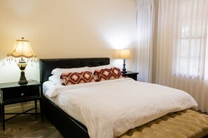 Une chambre d’hôtel avec un lit, deux tables de chevet, une lampe et une fenêtre avec des rideaux.