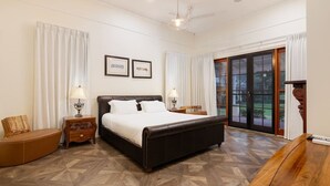 A bedroom with a large bed, two bedside tables with lamps, a wooden chair, and a view through a glass door.
