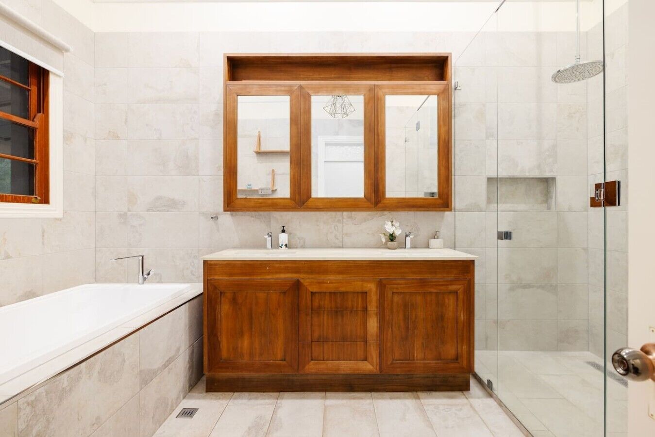 Ein Badezimmer mit einem Holzkosmetikschrank, einem großen Spiegel, einer Badewanne und einer Duschkabine aus Glas.