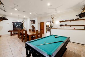 A room with a pool table, a dining table, and various decorative items including animal heads.