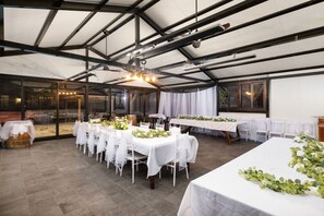 An indoor venue with tables set for a formal event, featuring a high ceiling and large windows.