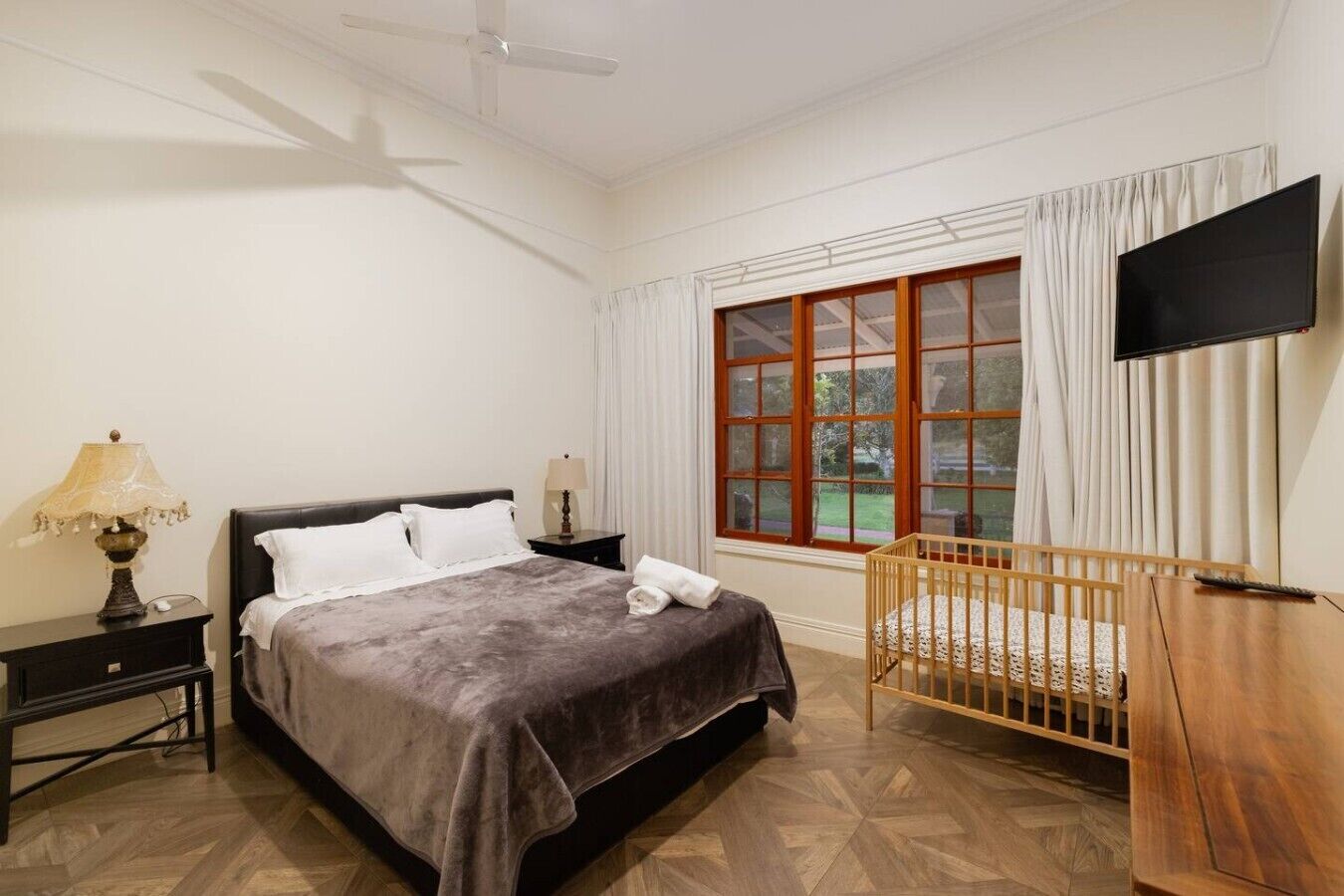 A hotel room with a bed, a crib, a TV, and a window with curtains.