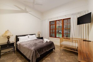 Ein Hotelzimmer mit Bett, Babybett, Fernseher und einem Fenster mit Vorhängen.