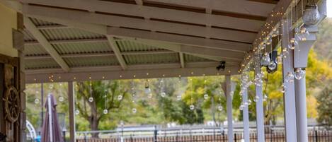An outdoor patio with a table and chairs, string lights, and a view of a park.