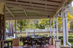 Un patio al aire libre con mesa y sillas, luces colgantes y vistas a un parque.