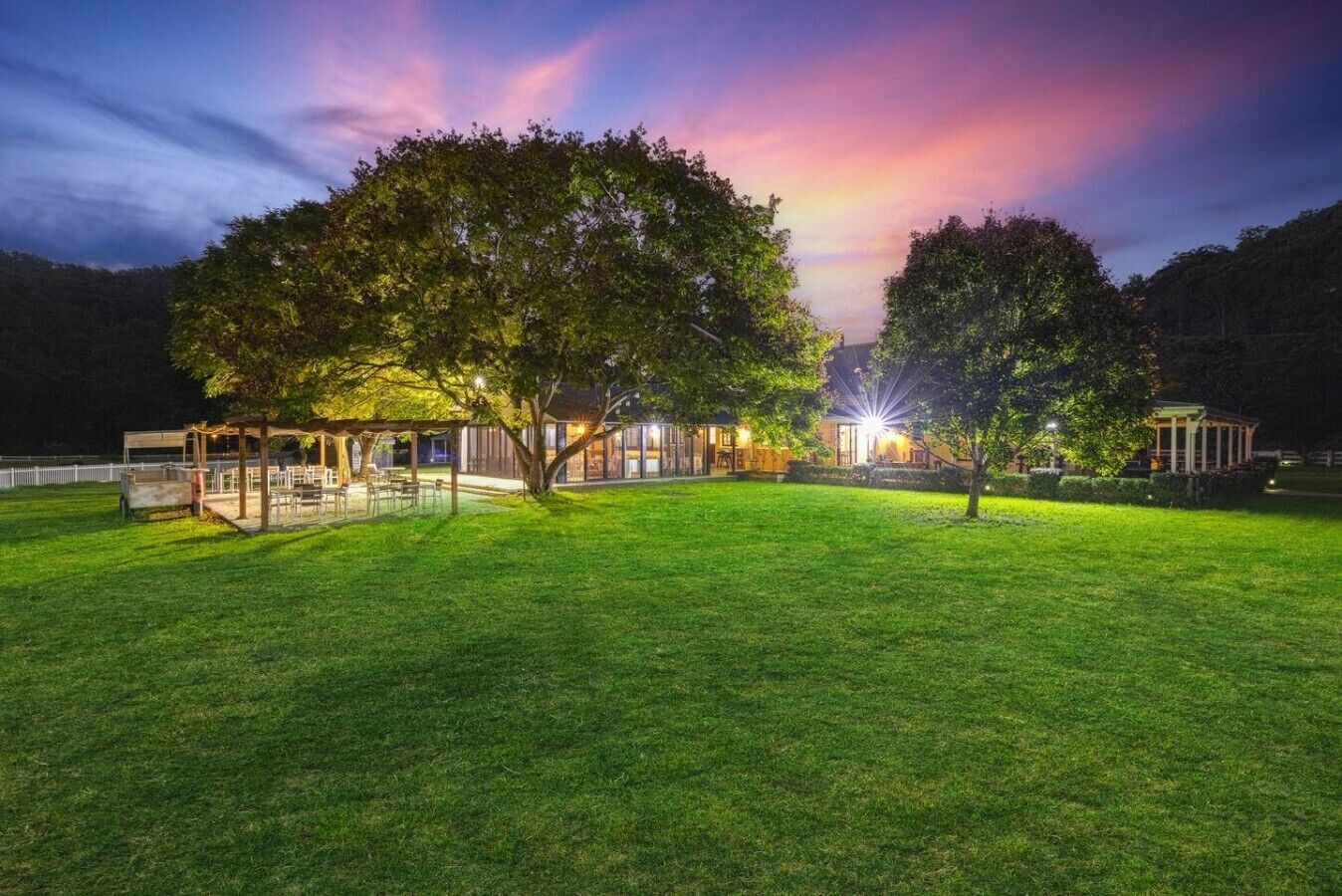 A well-lit outdoor area with a covered seating area, a lawn, and trees.