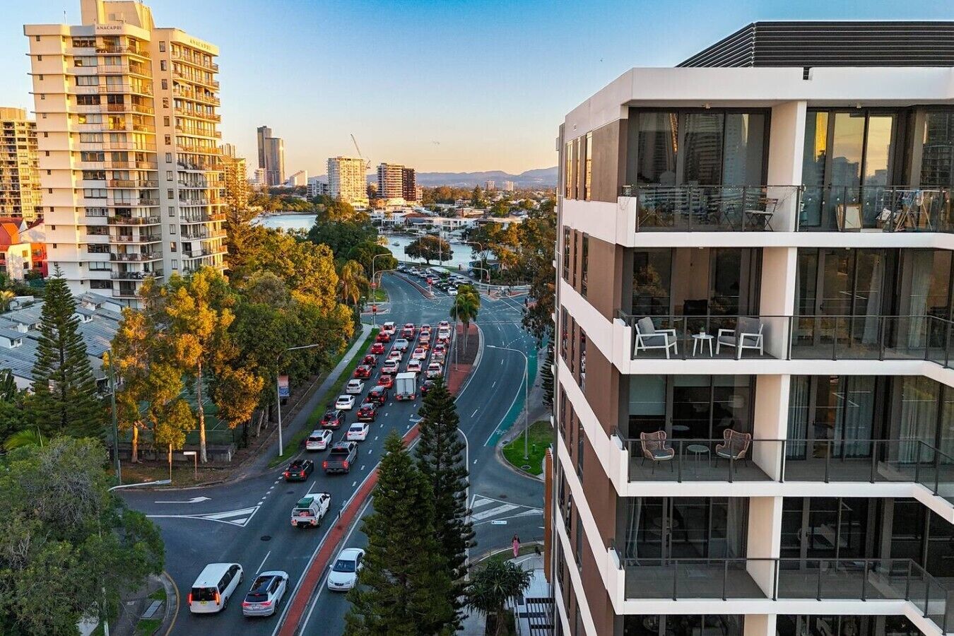 A multi-story building with balconies and large windows, situated next to a busy road with vehicles.
