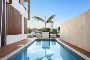 Ein moderner Pool im Freien mit Holzterrasse, Liegestühlen und einer Palme.