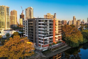 Ein mehrstöckiges Hotel mit Balkonen, ein Fluss im Vordergrund und eine Stadtansicht im Hintergrund.