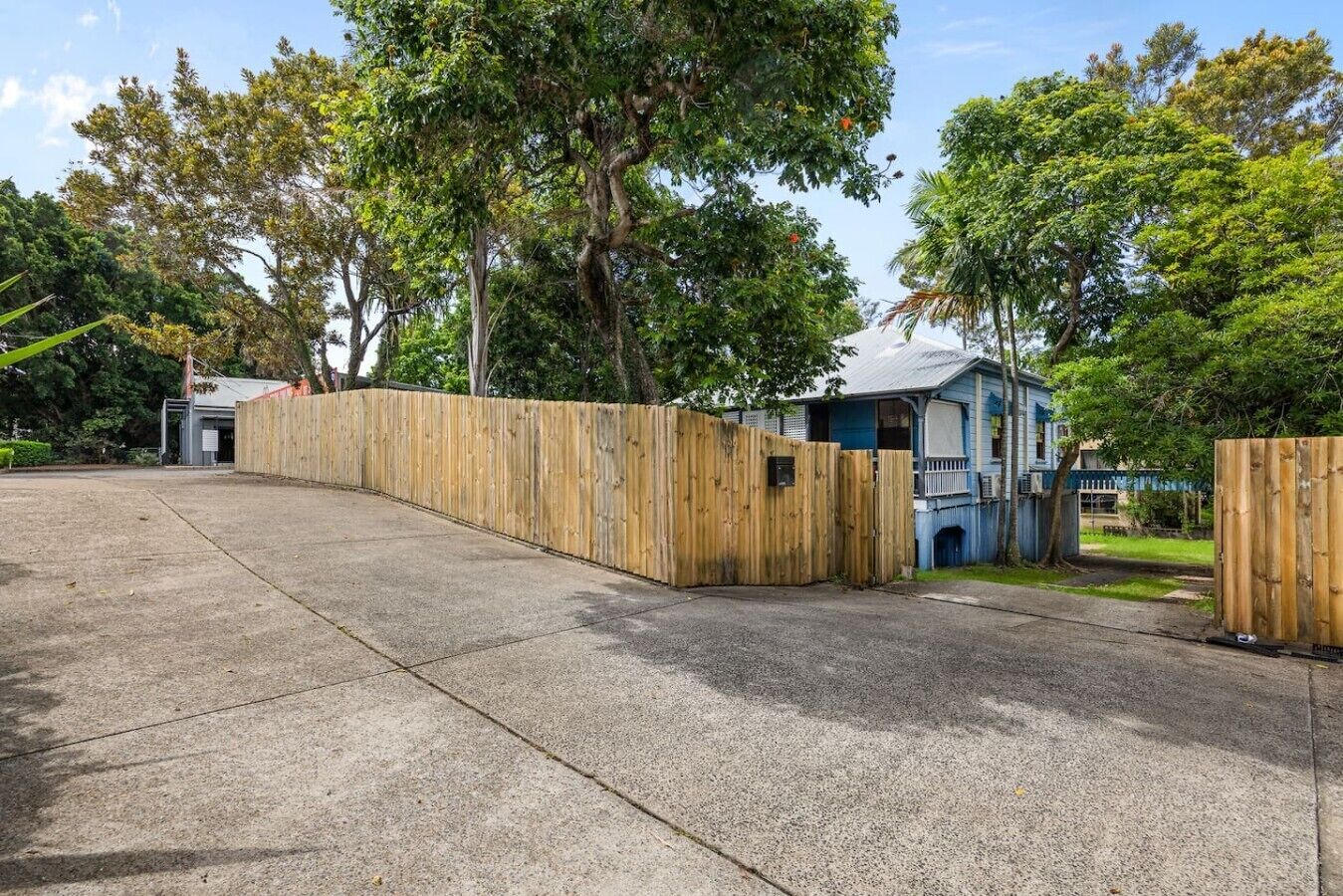 A residential property with a paved driveway, wooden fence, and a house with a blue exterior.