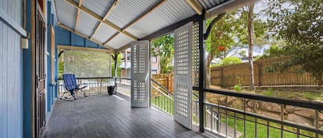 Un espacio al aire libre cubierto con una terraza de madera, una silla azul y vistas a un patio cercado.