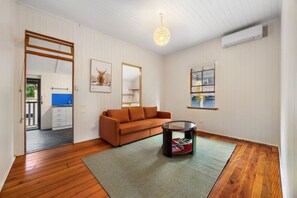 Una habitación con suelo de madera, un sofá, una mesa de centro, un espejo y una puerta que da a una cocina.