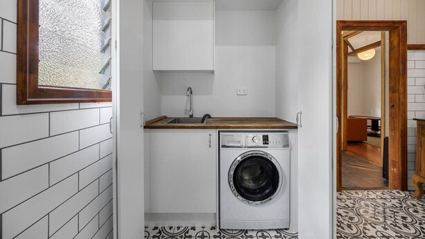 A compact laundry room with a washing machine, a sink, and cabinets.