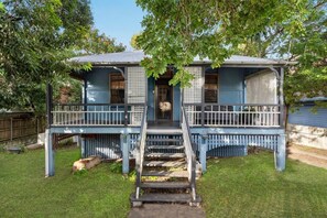 Ein zweistöckiges Haus mit Veranda, einer Treppe zum Eingang und einem umzäunten Garten.