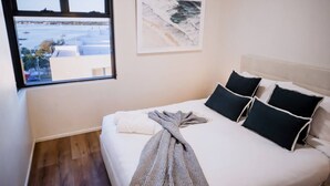 Una camera da letto con un letto, cuscini, una coperta, una finestra vista e un quadro appeso al muro.