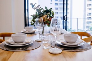 A dining table set with white bowls, plates, and glasses, with a vase of flowers in the center. - Broadwater 2 bed 2 Bath 1 CarPK&Beach&Parks (Southport)