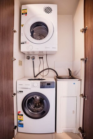 Une petite buanderie équipée d’un lave-linge à chargement frontal, d’un sèche-linge et d’un petit évier.