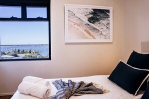 Une chambre d’hôtel avec un lit, une fenêtre donnant sur la mer et un tableau encadré au mur.