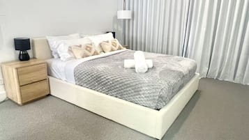 A modern bedroom with a bed, bedside tables, a ceiling fan, and a window with curtains.