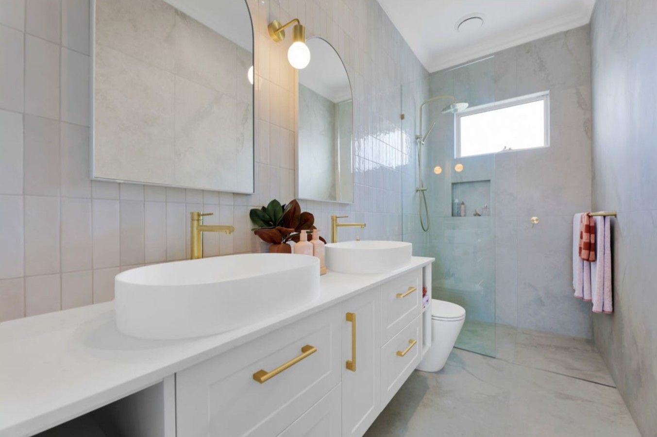 Un baño moderno con tocador blanco, detalles dorados y cabina de ducha de vidrio.