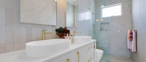 Un baño moderno con tocador blanco, detalles dorados y cabina de ducha de vidrio.