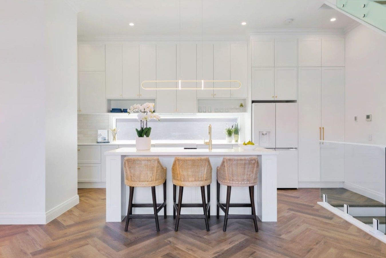 A modern kitchen with a central island, white cabinetry, and a herringbone wood floor.