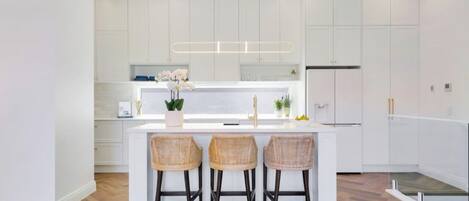 A modern kitchen with a central island, white cabinetry, and a herringbone wood floor.
