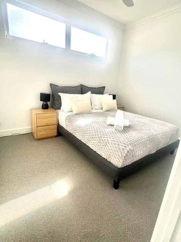 Un dormitorio con cama, mesita de noche, ventana y ventilador de techo.