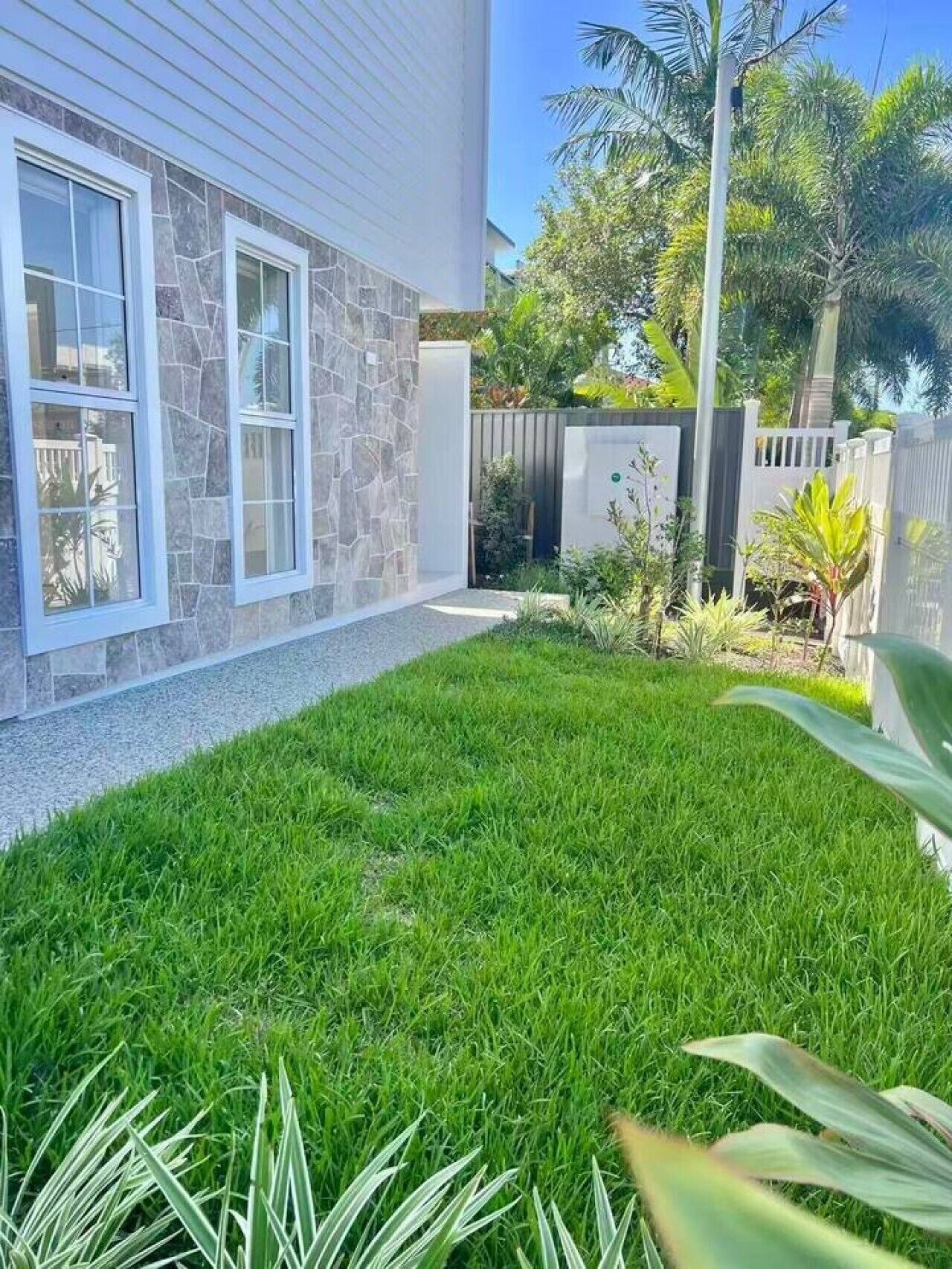 A residential property with a well-maintained lawn, a stone facade, and a fenced backyard.