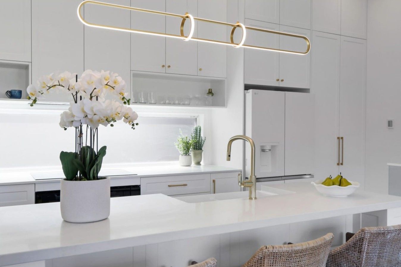 A modern kitchen with white cabinetry, a central island, a gold faucet, and a pendant light.