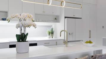 A modern kitchen with white cabinetry, a central island, a gold faucet, and a pendant light.