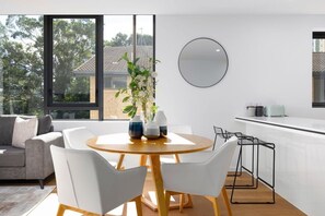 A modern kitchen with a round dining table, white chairs, and a large window. - Waterfront 2B 2Bath Pk,GYM,Pool&BBQ (Surfers Paradise)