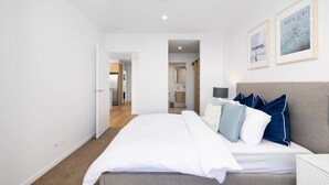 Um quarto moderno com uma cama grande, uma mesa de cabeceira e uma cabeceira. Há quadros nas paredes e uma porta que dá para um banheiro.