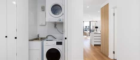 A modern laundry room with a front-loading washer and dryer, a sink, and a small countertop.