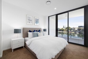 Een moderne slaapkamer met een groot bed, twee nachtkastjes, een nachtkast en uitzicht op een waterpartij door een schuifglazen deur.