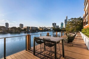 A waterfront deck with a table and chairs, overlooking a river with buildings in the background. - Waterfront 2B 2Bath Pk,GYM,Pool&BBQ (Surfers Paradise)