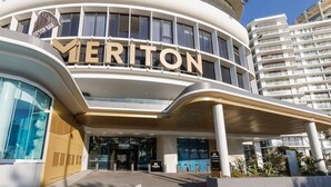 En modern hotellentrén med en framträdande skylt med texten ”MERITON”, en överbyggd gång och en glasfasad.