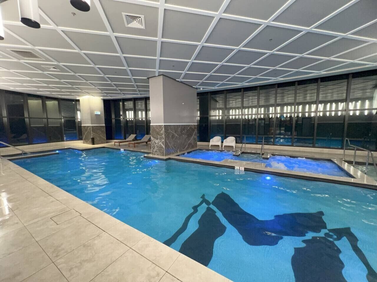 An indoor swimming pool with a tiled floor, a marble column, and a glass wall with windows.