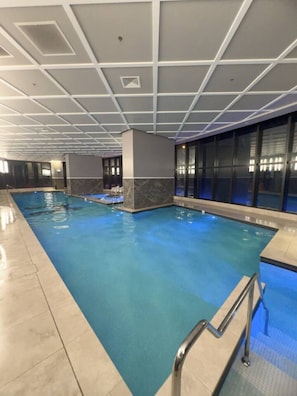 A large indoor swimming pool with clear water, surrounded by walls with a marble-like texture and a ceiling with a grid pattern. - New L63 Hill River CBD View&Pool & Sauna (Surfers Paradise)
