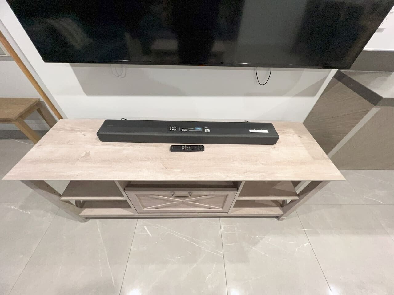 Un téléviseur à écran plat fixé au mur, au-dessus d’un meuble de rangement en bois, avec une télécommande.