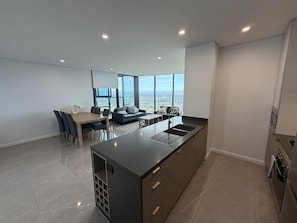 A modern kitchen with a central island, dining area with chairs, and a sofa. - New L63 Hill River CBD View&Pool & Sauna (Surfers Paradise)