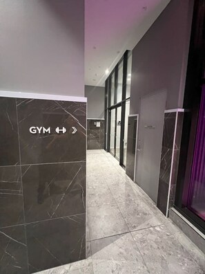 Ein Flur mit einem Hinweis auf einen Fitnessraum, Marmorboden und Glastüren.